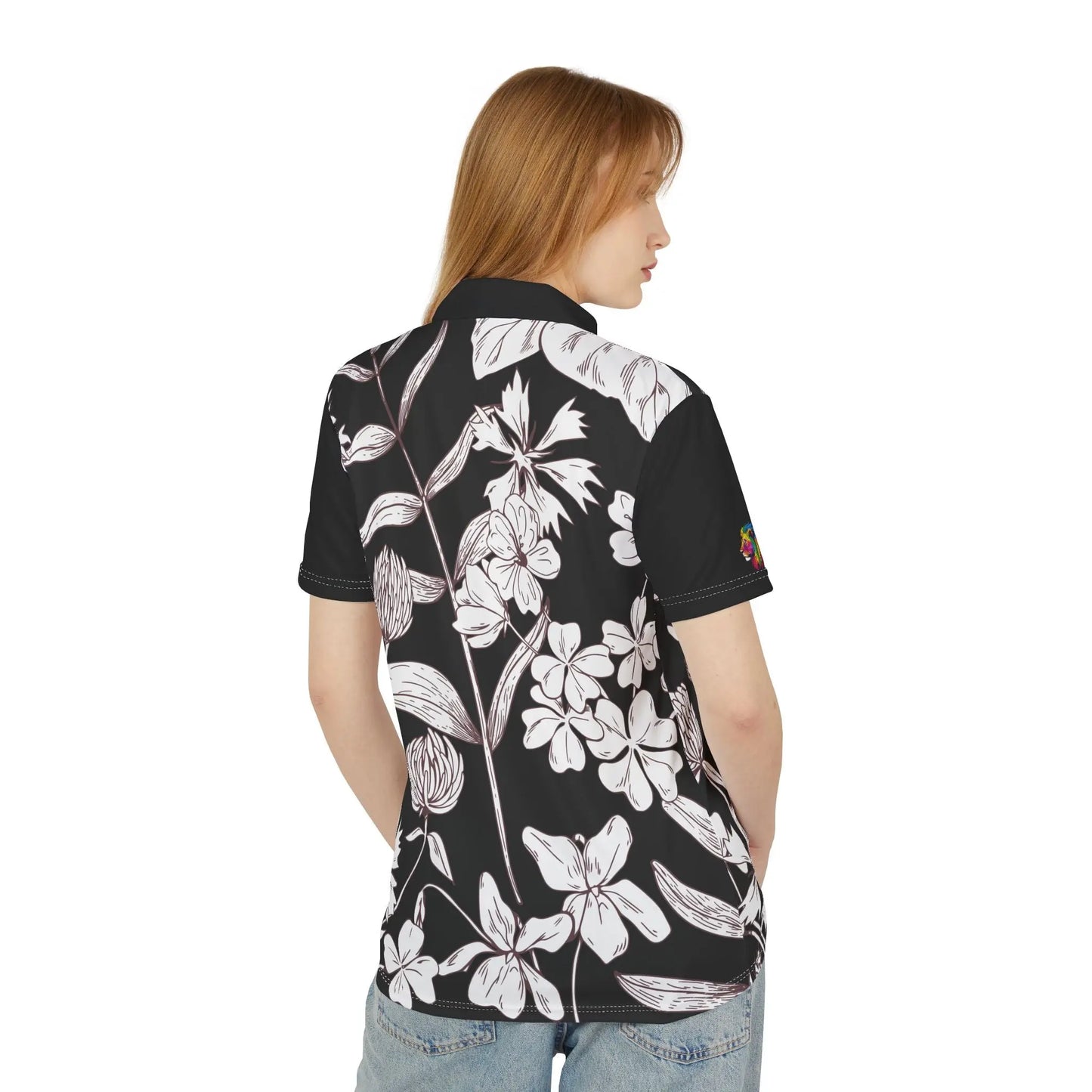 A person wears a black and white leaf and flower polo shirt from the Worldwide PRIDE Subtlety collection. On the right sleeve is a small colorful lion, an homage to the LBGTQ community. The person is placed against a plain white backdrop.