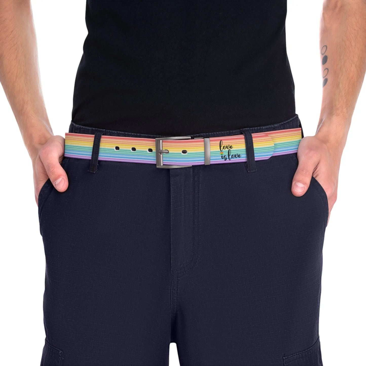 A person wearing a black shirt and black slacks with the Worldwide-PRIDE rainbow-striped Love is Love belt with gun metal buckle, showing support for the LGBTQ+ community, with one hand in their pocket.