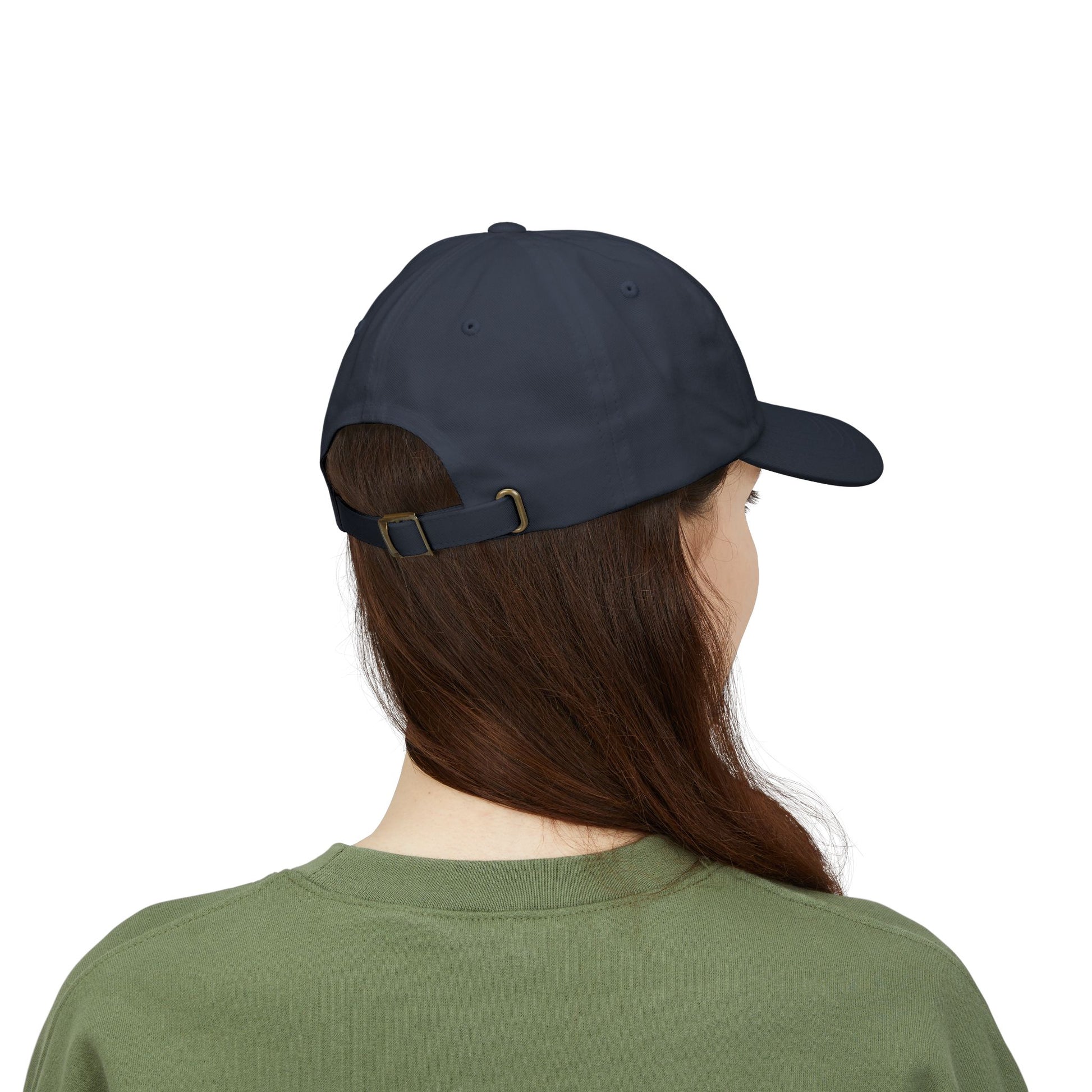 Back view of a person with long brown hair wearing a navy blue cap from the Worldwide PRIDE store, featuring a rainbow design and the embroidered pronouns she/her, along with an olive green sweatshirt. 