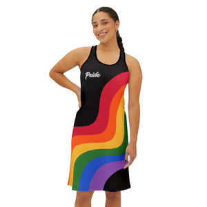 A smiling person wearing a sleeveless black racerback dress adorned with colorful rainbow stripes and the word Pride boldly across the chest. They stand confidently with one hand on their hip against a plain white background, celebrating Worldwide PRIDE.