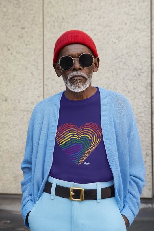 Man wearing a blue cardigan, purple shirt with rainbow fingerprint heart design, red beanie, and sunglasses against a textured wall.