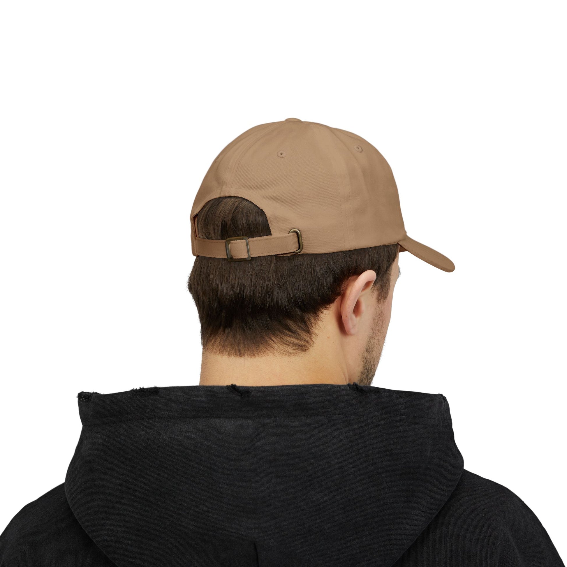 Back view of a person with short brown hair wearing a khaki cap from the Worldwide PRIDE store, featuring a rainbow design and the embroidered pronouns he/him. The person is also wearing a black hooded sweatshirt and looking down.