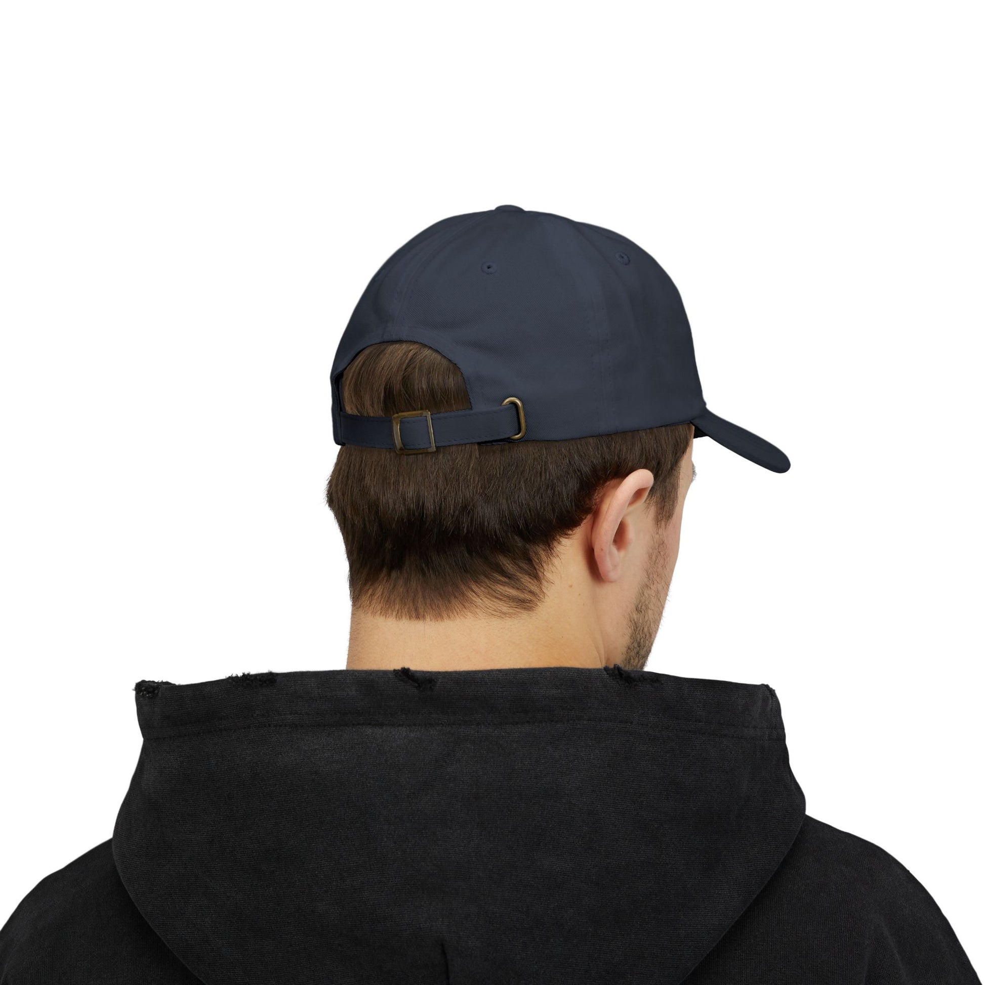 Back view of a person with short brown hair wearing a navy blue cap from the Worldwide PRIDE store, featuring a rainbow design and the embroidered pronouns he/him. The person is also wearing a black hooded sweatshirt and looking down.