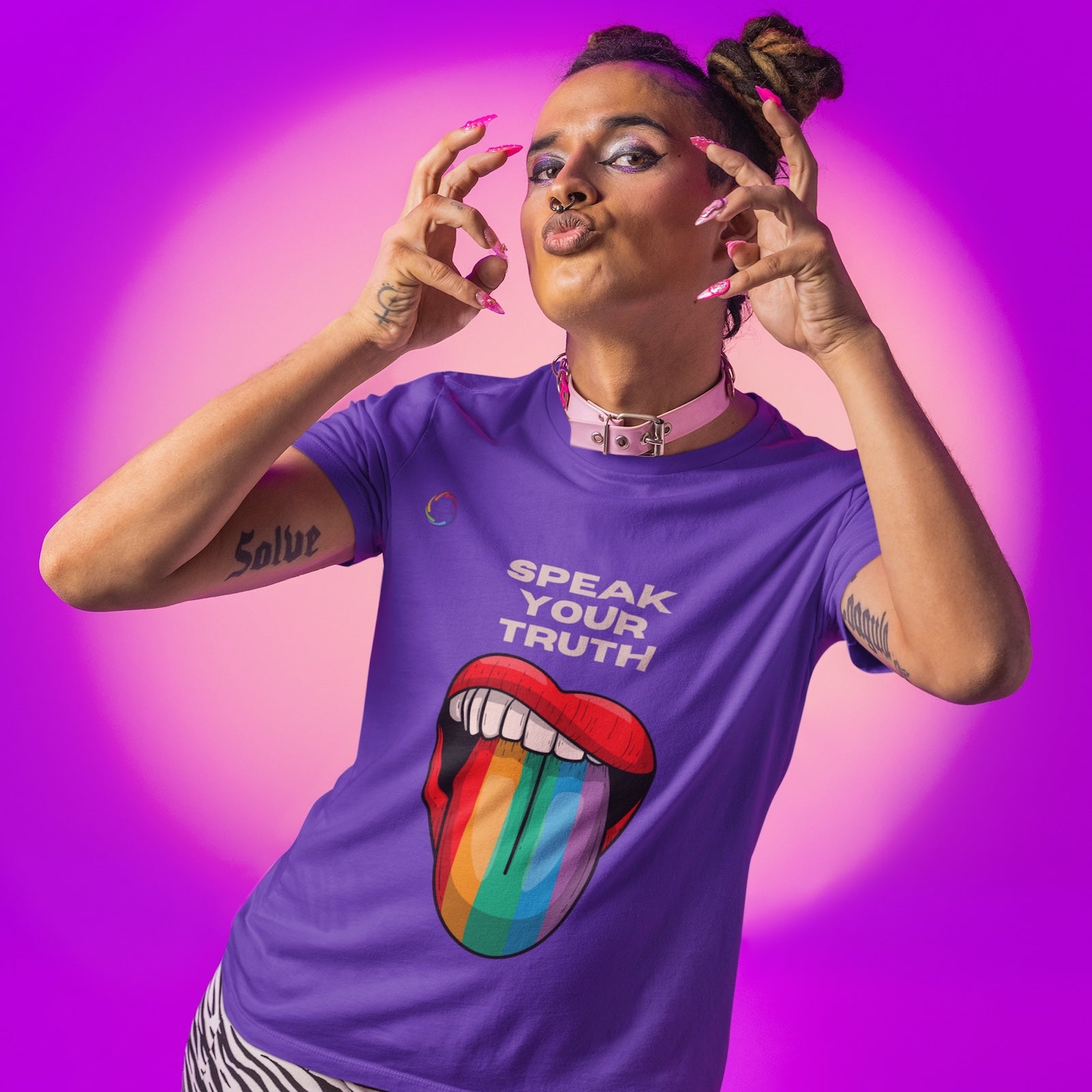 Person with braided hair poses confidently against a vibrant purple background. Embracing the Worldwide PRIDE spirit, they wear a purple t-shirt with a rainbow-colored mouth design and the words SPEAK YOUR TRUTH, along with zebra-print pants and colorful makeup, celebrating the LGBTQ community.