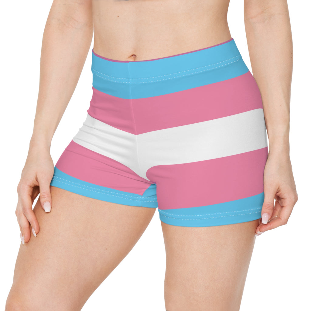 A person wearing colorful shorts with pink, blue, and white horizontal stripes echoes the design of the transsexual flag. Seen from the front, their hand casually rests on their hip, showcasing pride and style in one striking look.