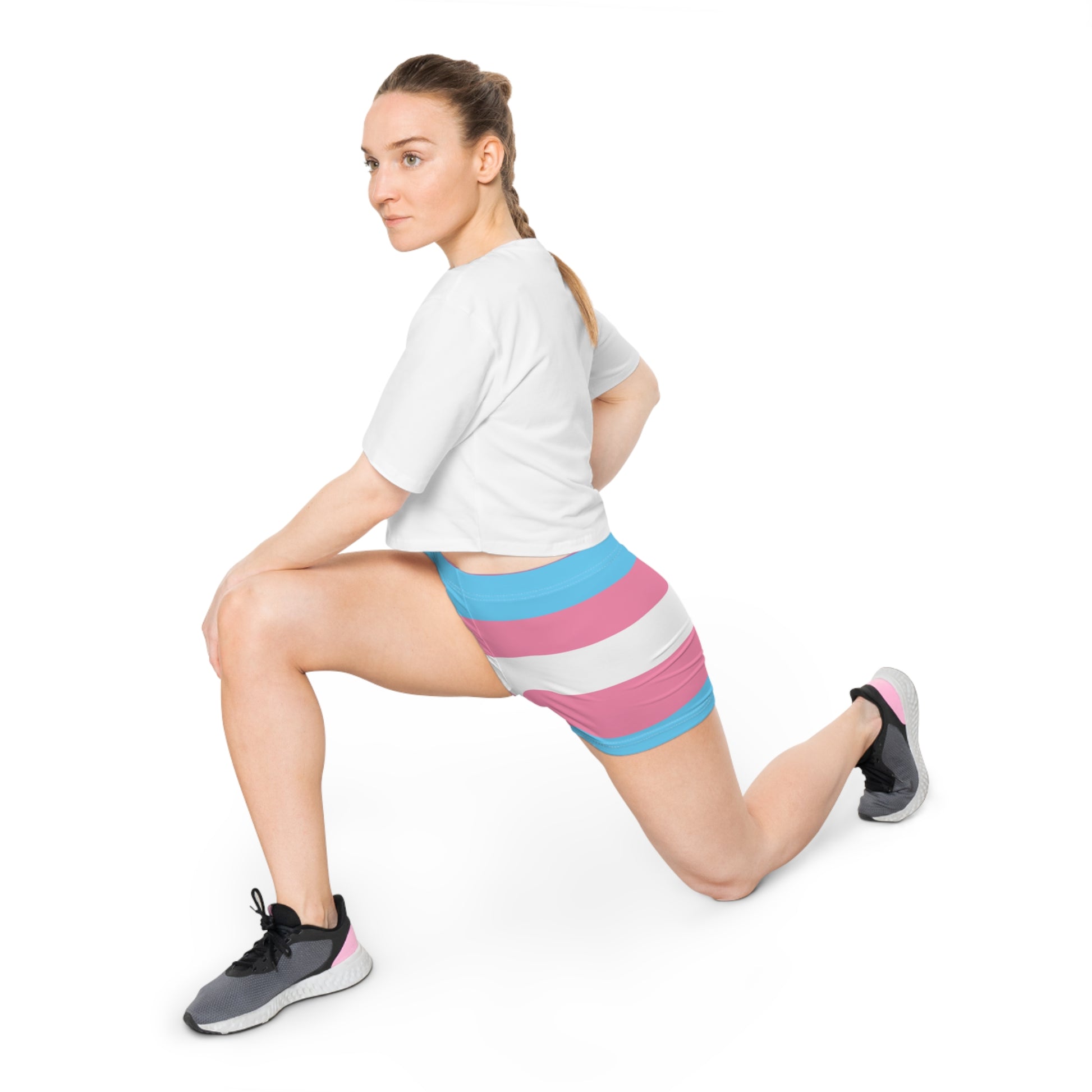 A person kneels on one knee wearing colorful shorts with pink, blue, and white horizontal stripes echoes the design of the transsexual flag. Seen from the side, their hand casually rests on their knee, showcasing pride and style in one striking look.