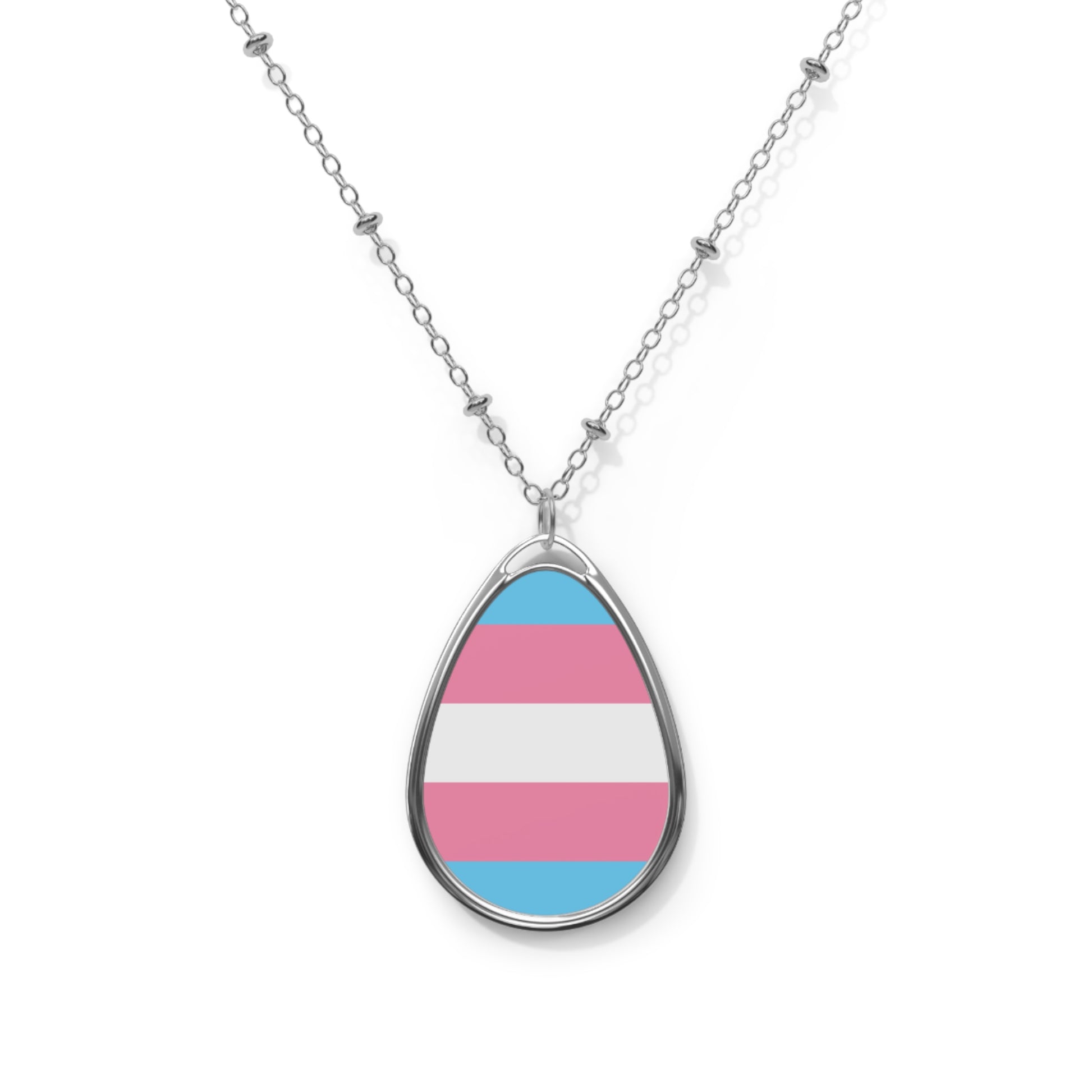 Close up of a teardrop shaped necklace proudly displaying the colors and design of the transsexual flag. The necklace hangs on a glass box. The carolina blue, pink and white colors symbolize the struggle and plight of the Trans community.