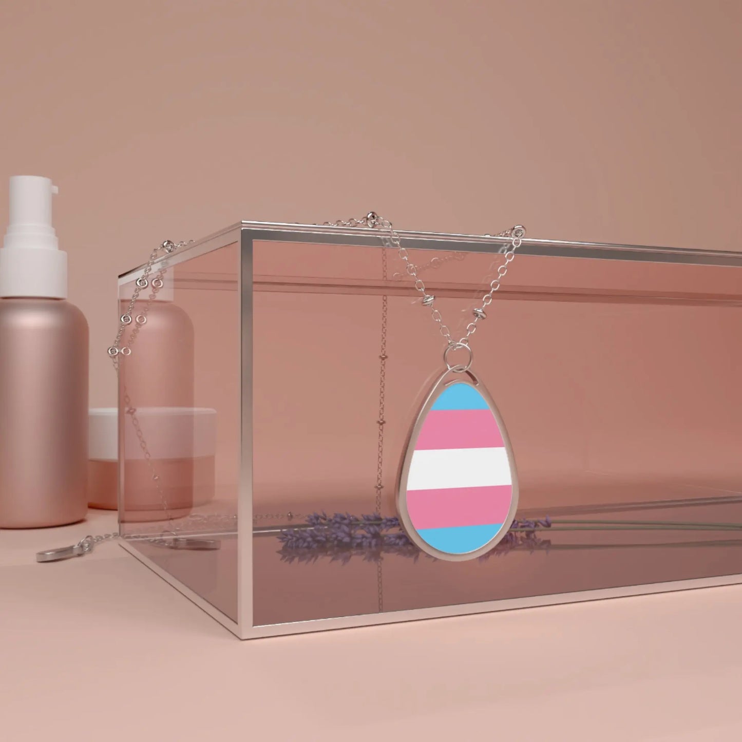 Close up of a teardrop-shaped  necklace proudly displaying the colors and design of the transsexual flag. The necklace hangs on a glass box. The carolina blue, pink and white colors symbolize the struggle and plight of the Trans community.