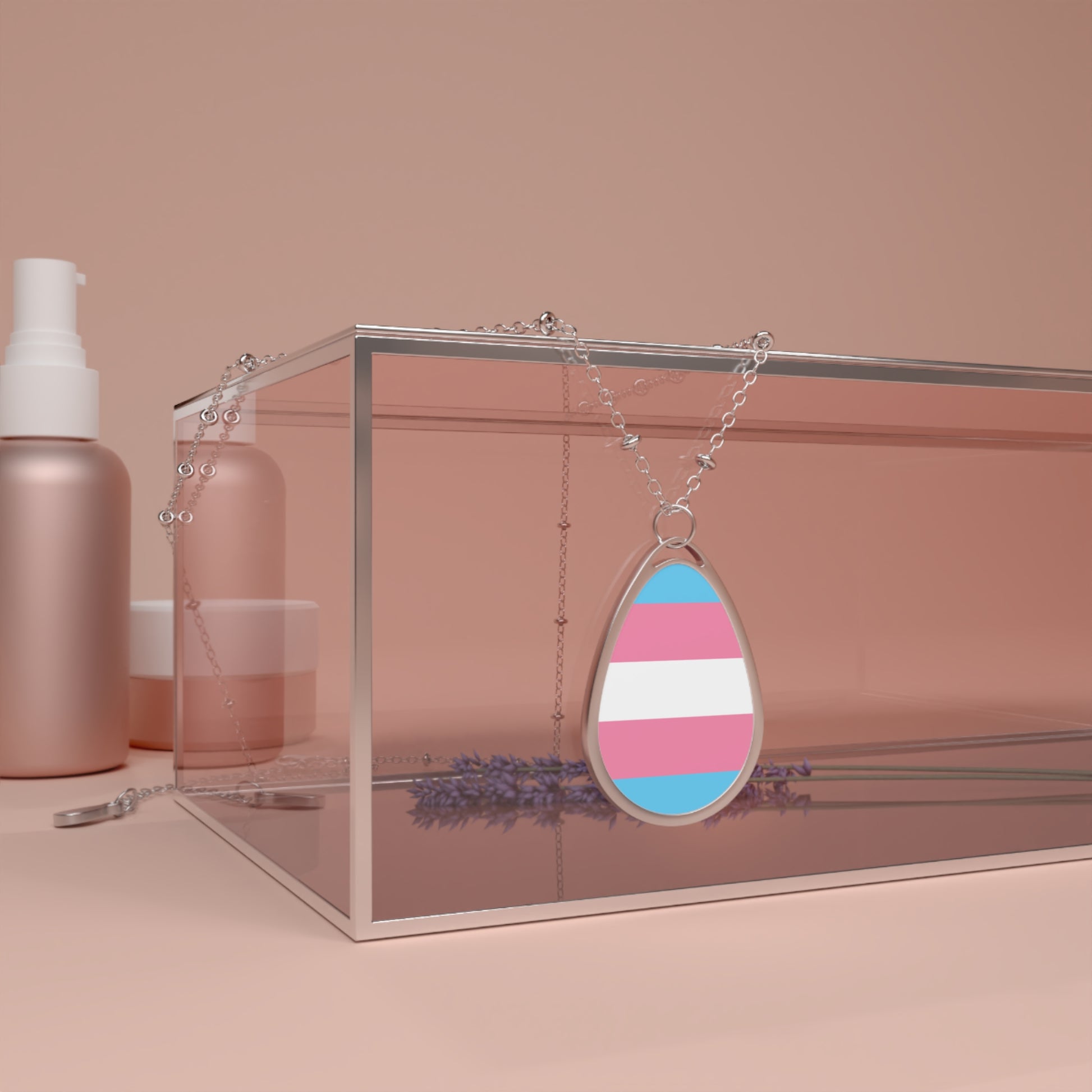 Close up of a teardrop-shaped  necklace proudly displaying the colors and design of the transsexual flag. The necklace hangs on a glass box. The carolina blue, pink and white colors symbolize the struggle and plight of the Trans community.