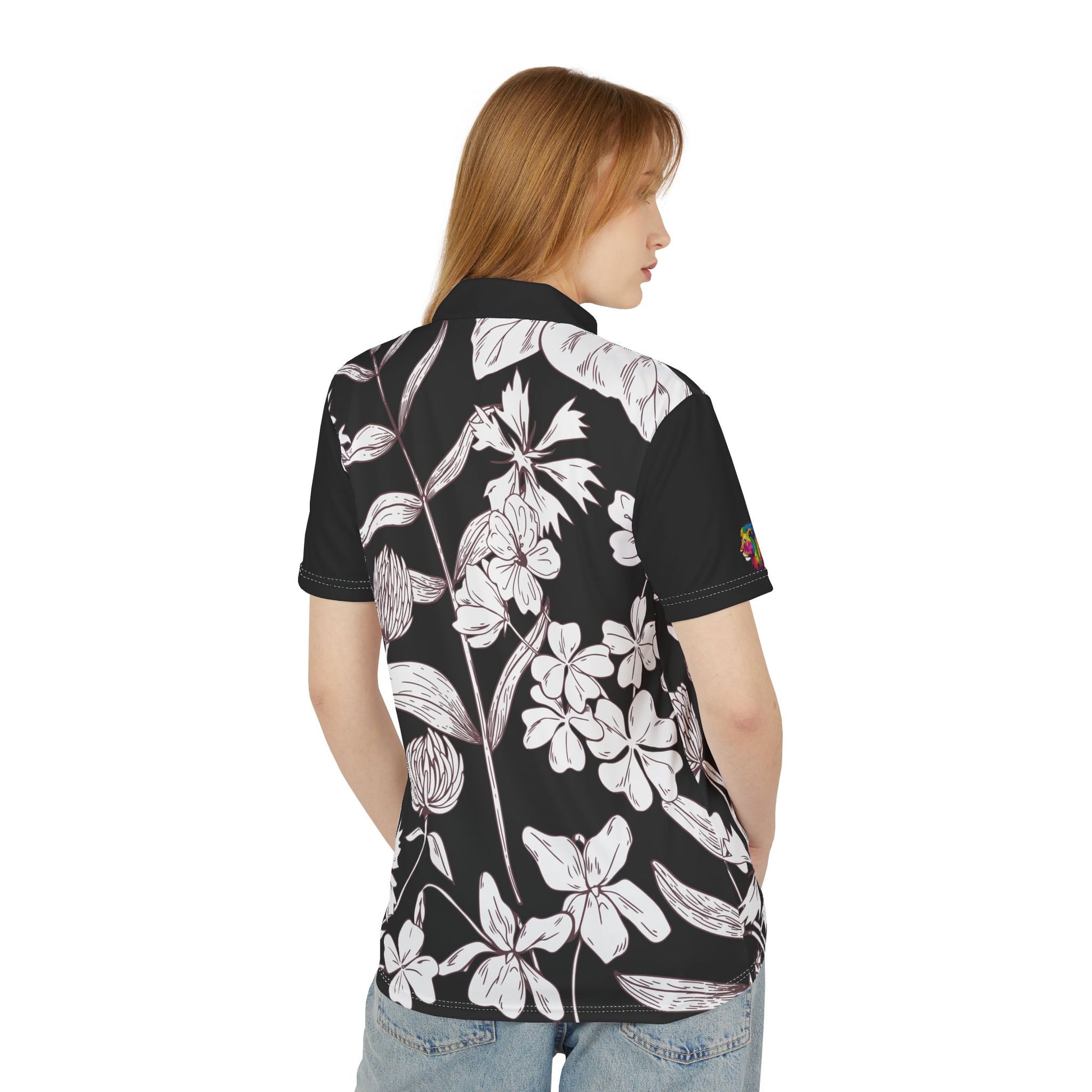 A person wears a black and white leaf and flower polo shirt from the Worldwide PRIDE Subtlety collection. On the right sleeve is a small colorful lion, an homage to the LBGTQ community. The person is placed against a plain white backdrop.