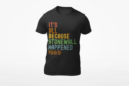 A black unisex short-sleeve t-shirt with the text 'IT'S ALL BECAUSE STONEWALL HAPPENED' printed in bold, multicolored letters.