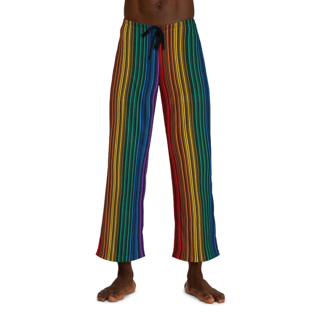 A person wearing colorful striped pants featuring vertical rainbow lines stands barefoot against a plain white background. Embracing the spirit of Worldwide PRIDE, these pants, with their drawstring waist, reflect the vibrant energy of the LGBTQ community. The persons upper body is not visible.