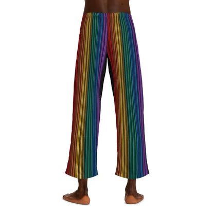 A person wearing colorful striped pants featuring vertical rainbow lines stands barefoot against a plain white background. Embracing the spirit of Worldwide PRIDE, these pants, with their drawstring waist, reflect the vibrant energy of the LGBTQ community. The persons upper body is not visible.