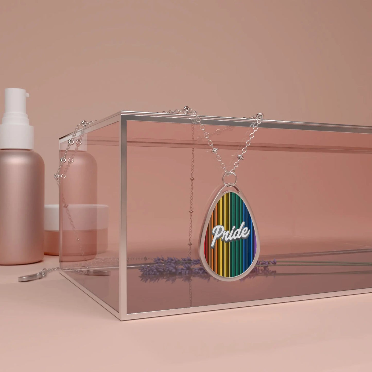 A silver chain necklace showcases a teardrop-shaped pendant adorned with a rainbow-striped pattern and the word PRIDE in elegant white cursive. The necklace hangs over a glass box. The close-up captures the vibrant colors and shiny metal beautifully.