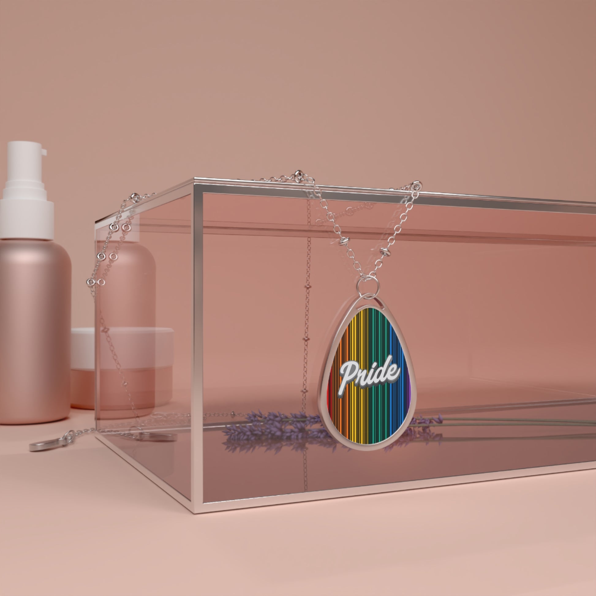 A silver chain necklace showcases a teardrop-shaped pendant adorned with a rainbow-striped pattern and the word PRIDE in elegant white cursive. The necklace hangs over a glass box. The close-up captures the vibrant colors and shiny metal beautifully.