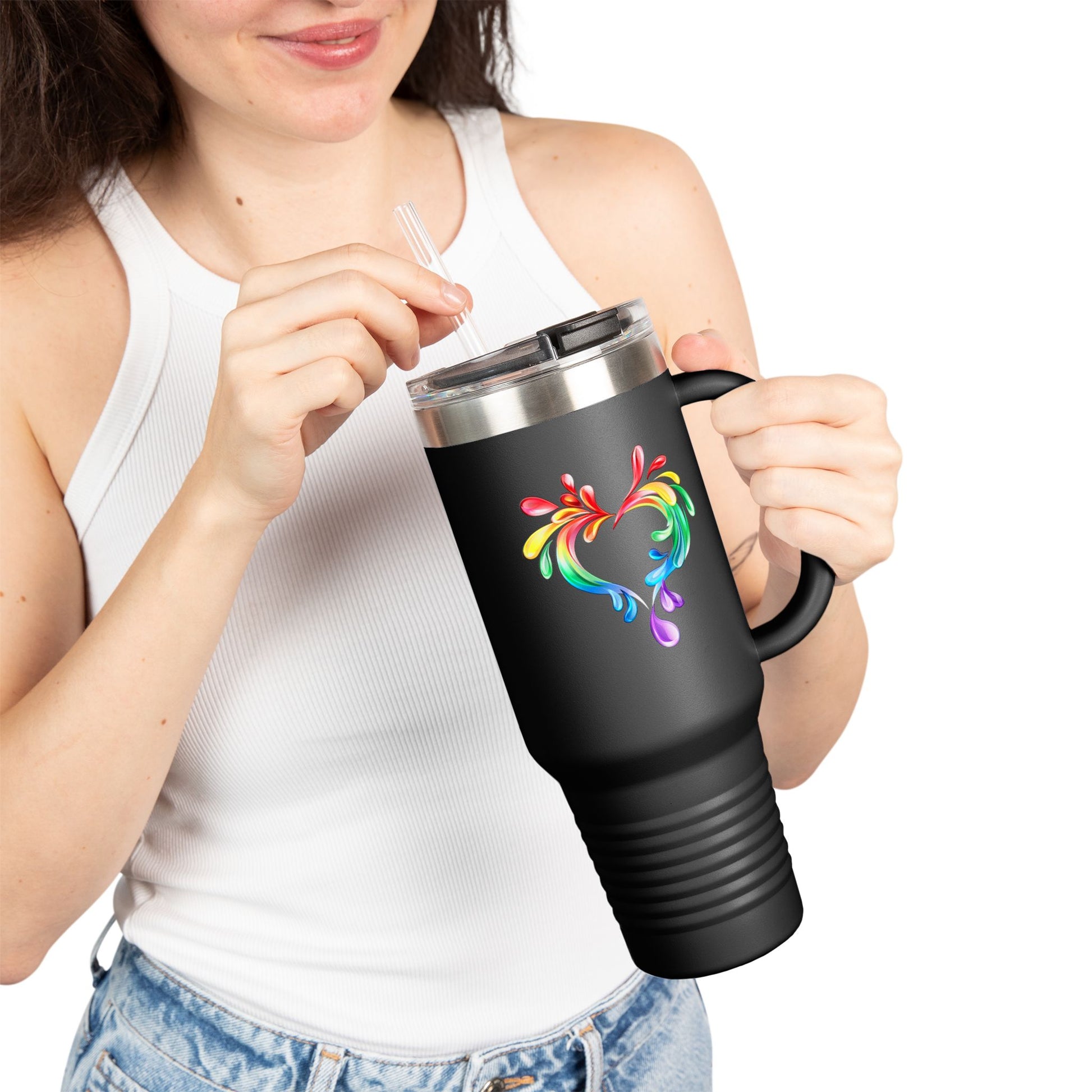 A person holds a black travel mug with a handle and straw, showcasing a colorful heart made of water splashes. The Worldwide PRIDE cup is celebrating diversity and love.