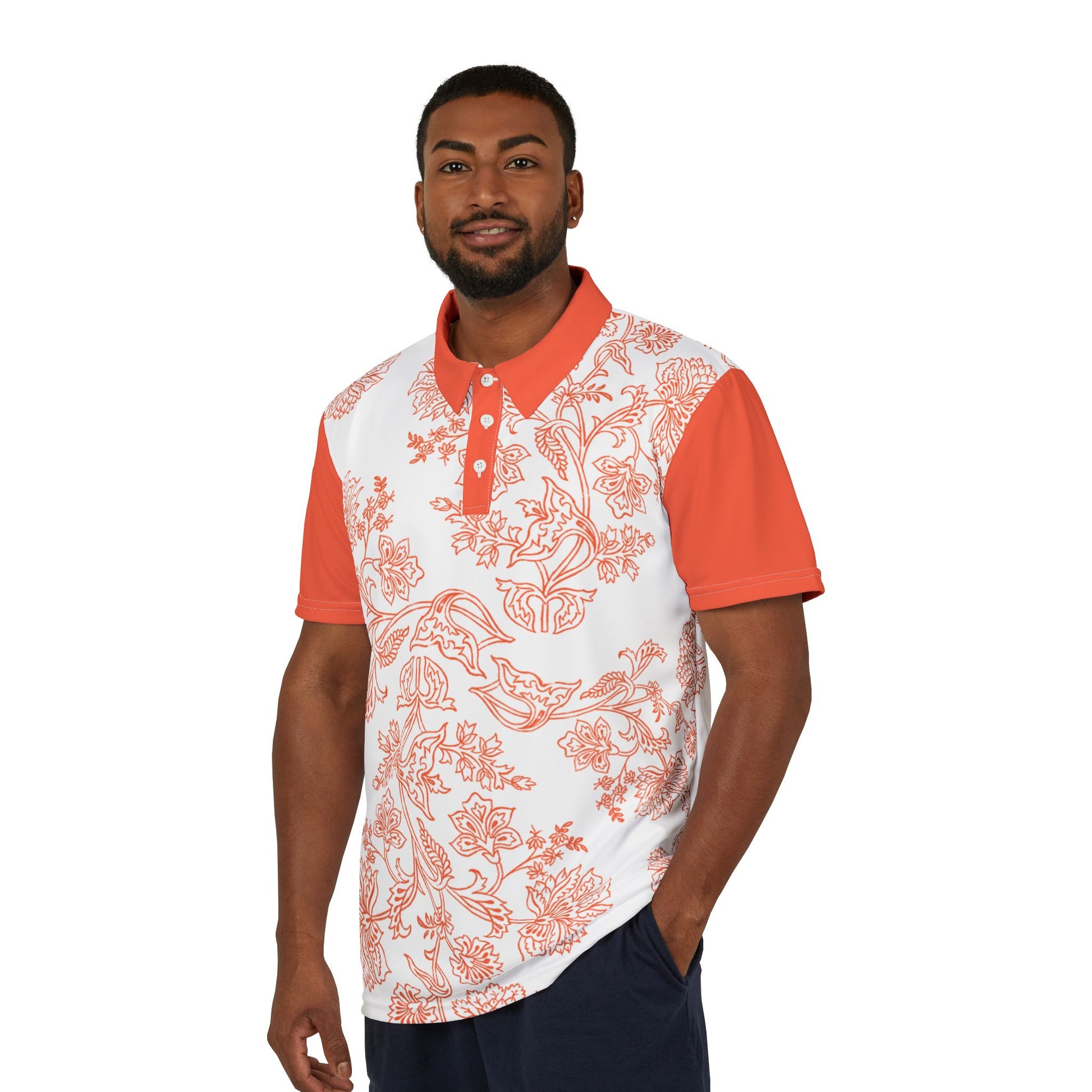 A person wears an orange and white paisley flower polo shirt from the Worldwide PRIDE Subtlety collection. On the right sleeve is a small colorful lion, an homage to the LBGTQ community. The person is placed against a plain white backdrop.