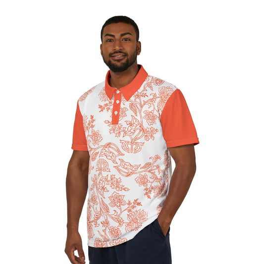 A person wears an orange and white paisley flower polo shirt from the Worldwide PRIDE Subtlety collection. On the right sleeve is a small colorful lion, an homage to the LBGTQ community. The person is placed against a plain white backdrop.