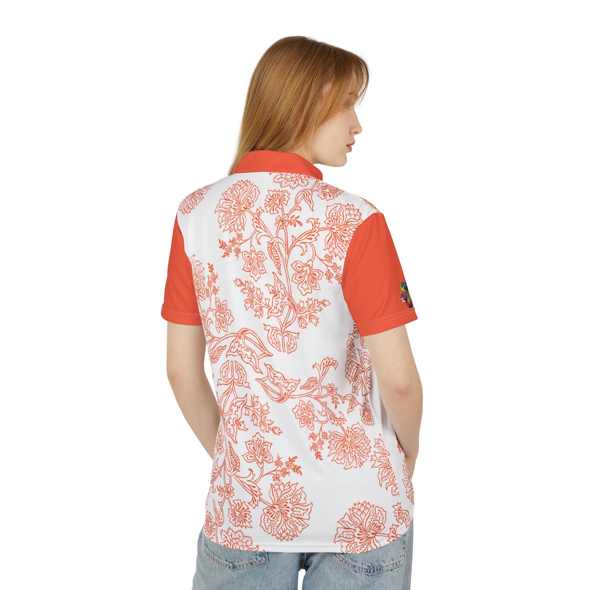 A person wears an orange and white paisley flower polo shirt from the Worldwide PRIDE Subtlety collection. On the right sleeve is a small colorful lion, an homage to the LBGTQ community. The person is placed against a plain white backdrop.