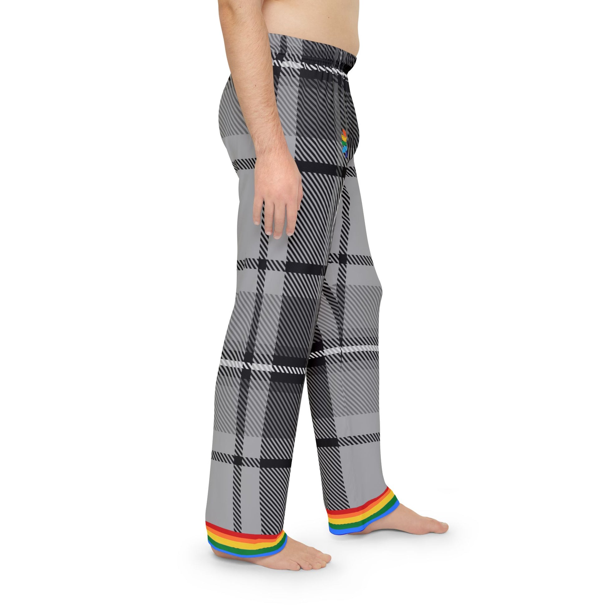 A person is standing barefoot, wearing gray and black plaid pants with a rainbow trim at the cuffs. The persons torso is not covered by any clothing. The pants feature a subtle rainbow detail near the waistband. The background is plain white.