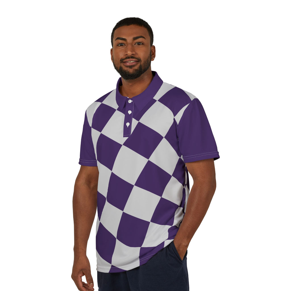 A man wearing a purple and white checkered polo shirt from the Worldwide PRIDE Subtlety collection stands with his left hand in his pocket, smiling. On the right sleeve is a small colorful lion, an homage to the LBGTQ community. He is placed against a plain white backdrop.