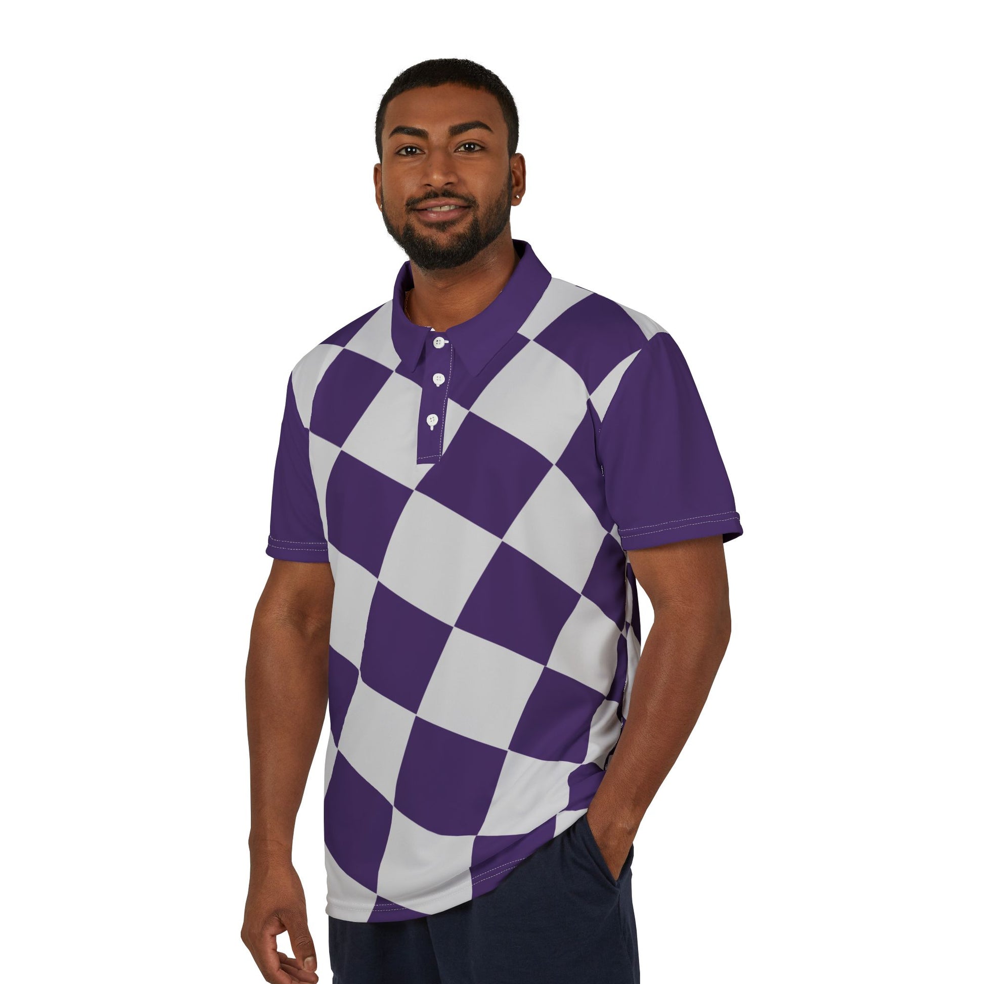 A man wearing a purple and white checkered polo shirt from the Worldwide PRIDE Subtlety collection stands with his left hand in his pocket, smiling. On the right sleeve is a small colorful lion, an homage to the LBGTQ community. He is placed against a plain white backdrop.
