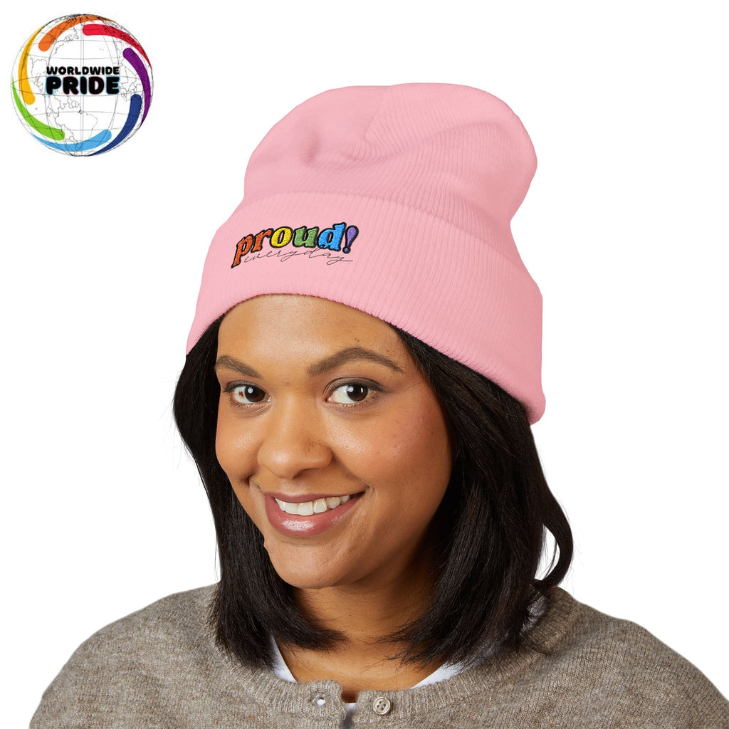 A person wearing a light pink beanie with “proud everyday" embroidered in rainbow colors and a heather brown sweater, looking slightly to the side with a neutral expression. Perfect for the LGBTQ community from the Worldwide PRIDE store.
