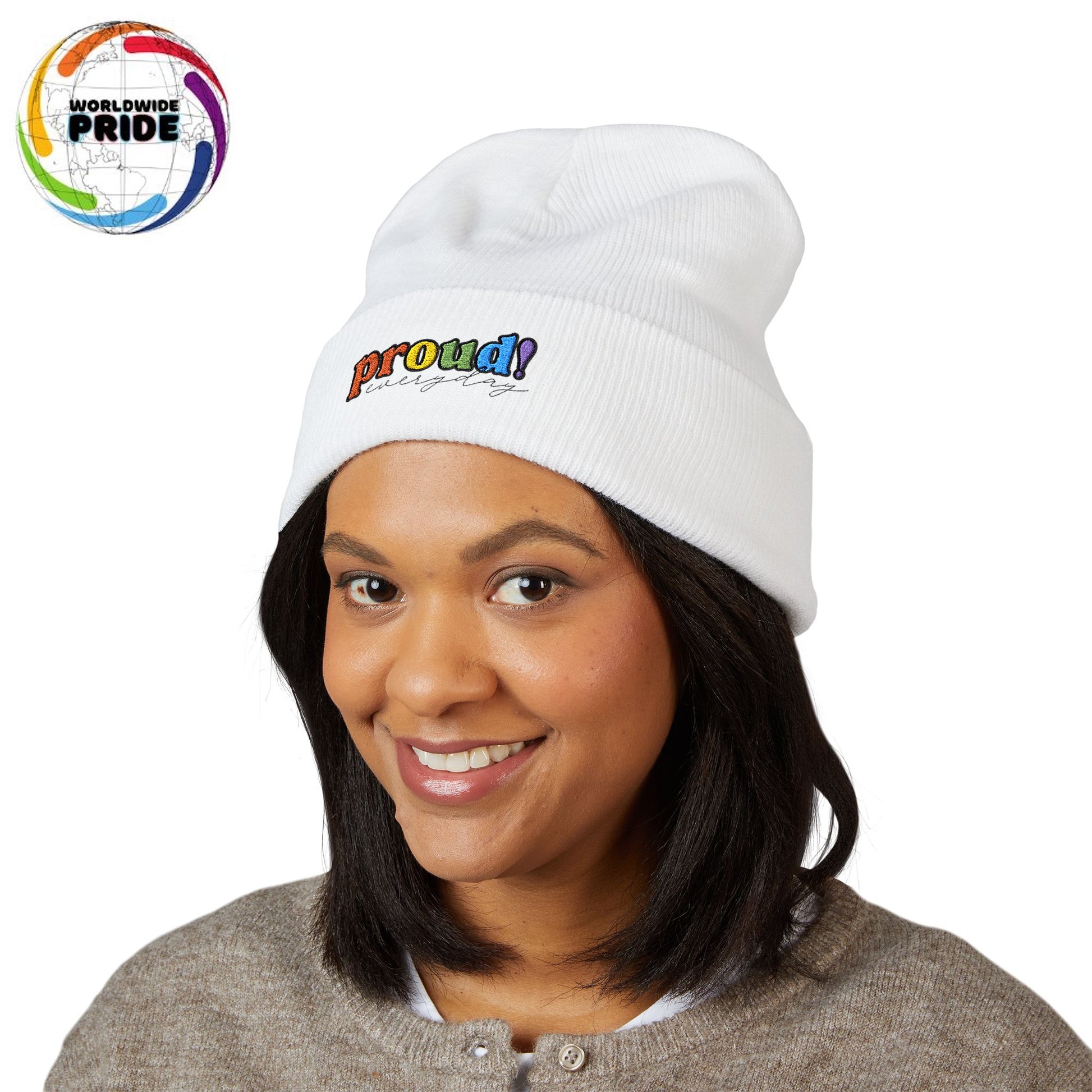 A person wearing a white beanie with “proud everyday" embroidered in rainbow colors and a heather brown sweater, looking slightly to the side with a neutral expression. Perfect for the LGBTQ community from the Worldwide PRIDE store.