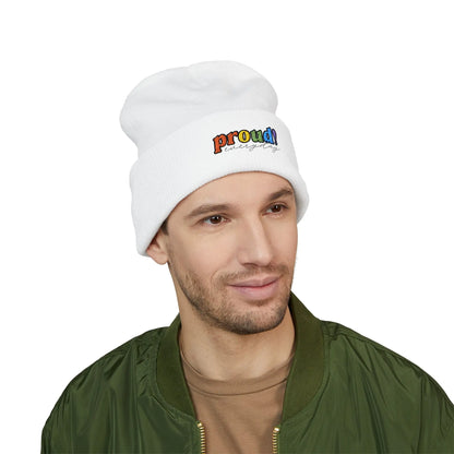 A person wearing a white beanie with “proud everyday" embroidered in rainbow colors and a green jacket, looking slightly to the side with a neutral expression. Perfect for the LGBTQ community from the Worldwide PRIDE store.