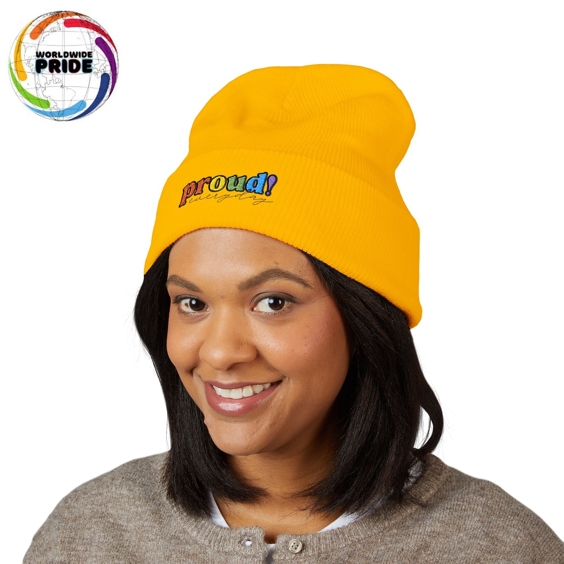 A person wearing a yellow beanie with “proud everyday" embroidered in rainbow colors and a heather brown sweater, looking slightly to the side with a neutral expression. Perfect for the LGBTQ community from the Worldwide PRIDE store.