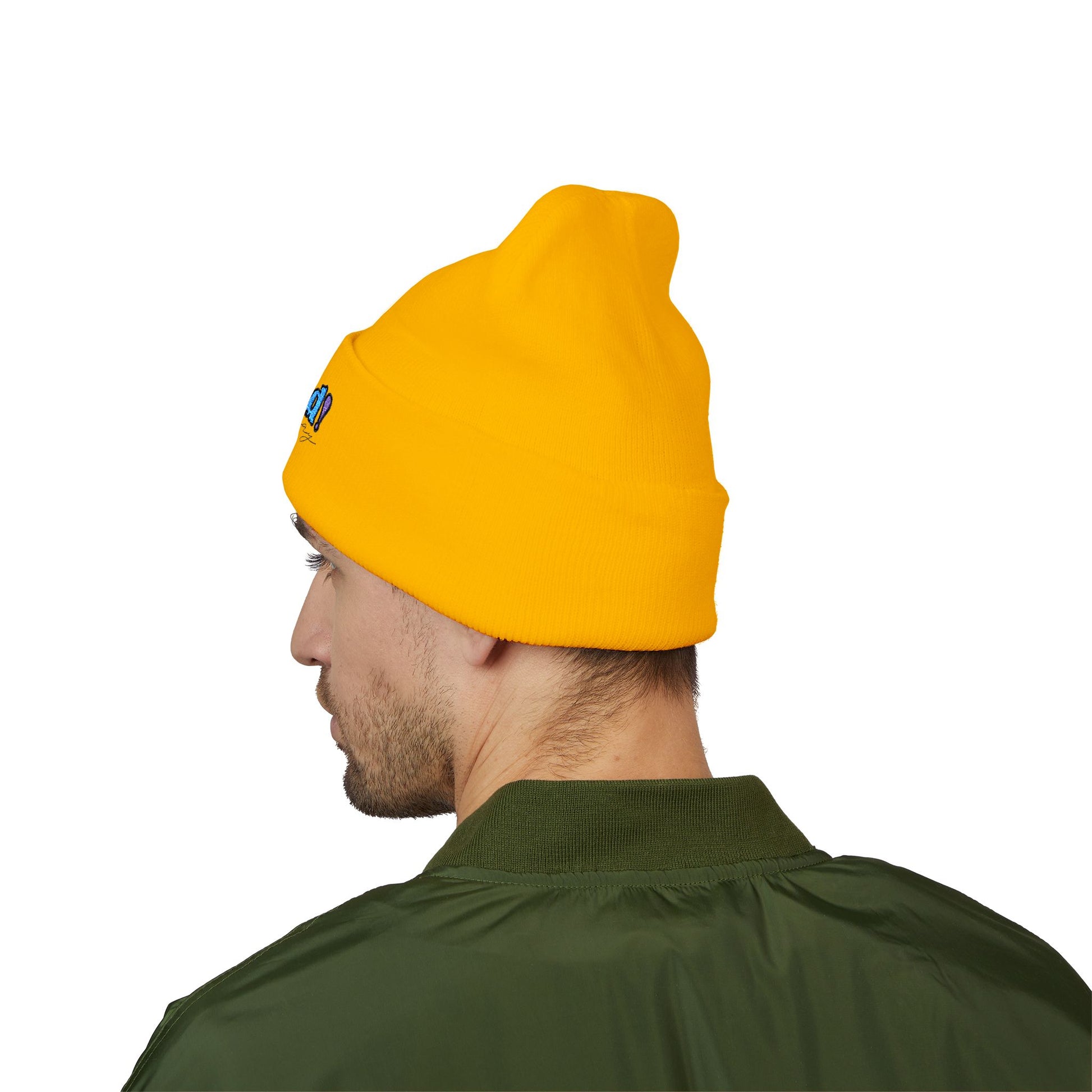 Back view of a person wearing a yellow beanie with “proud everyday" embroidered in rainbow colors and a green jacket, looking slightly to the side with a neutral expression. Perfect for the LGBTQ community from the Worldwide PRIDE store.