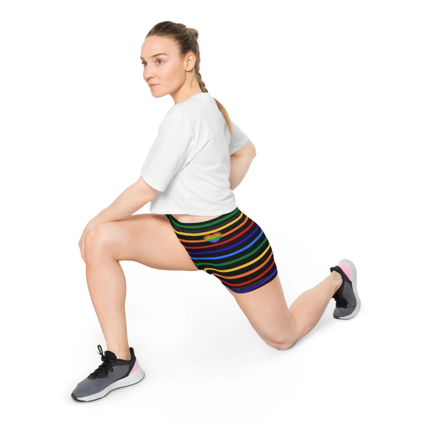 A person wearing a pair of women's shorts featuring a striped pattern a glittery heart, and vibrant rainbow colors on a black background.