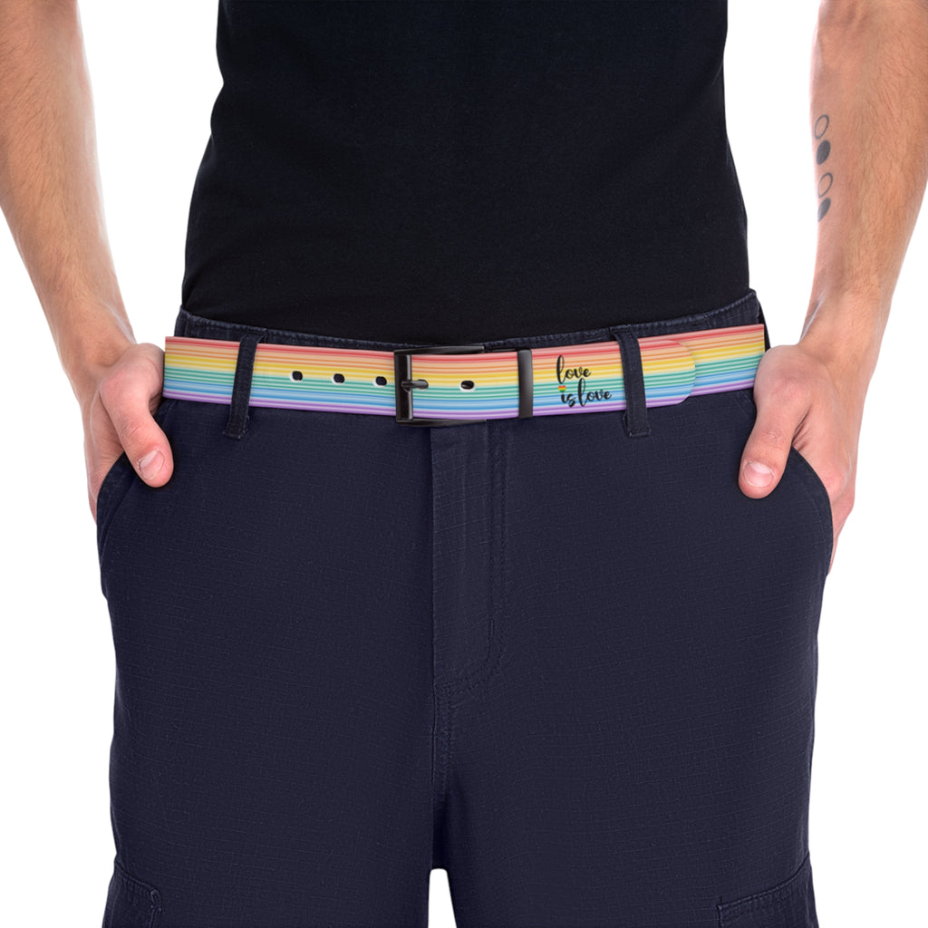 A person wearing a black shirt and black slacks with the Worldwide-PRIDE rainbow-striped Love is Love belt with black buckle, showing support for the LGBTQ+ community, with one hand in their pocket.