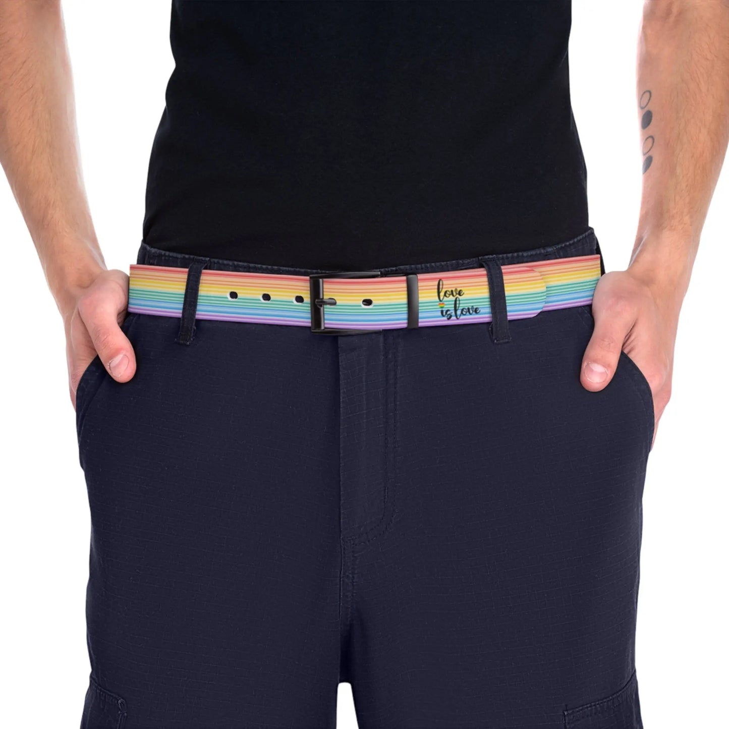 A person wearing a black shirt and black slacks with the Worldwide-PRIDE rainbow-striped Love is Love belt with black buckle, showing support for the LGBTQ+ community, with one hand in their pocket.