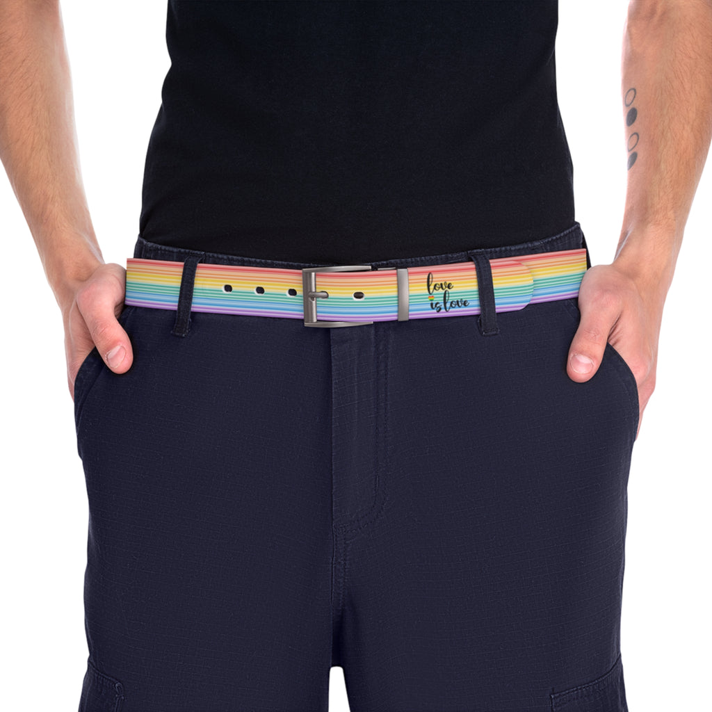 A person wearing a black shirt and black slacks with the Worldwide-PRIDE rainbow-striped Love is Love belt with gun metal buckle, showing support for the LGBTQ+ community, with one hand in their pocket.