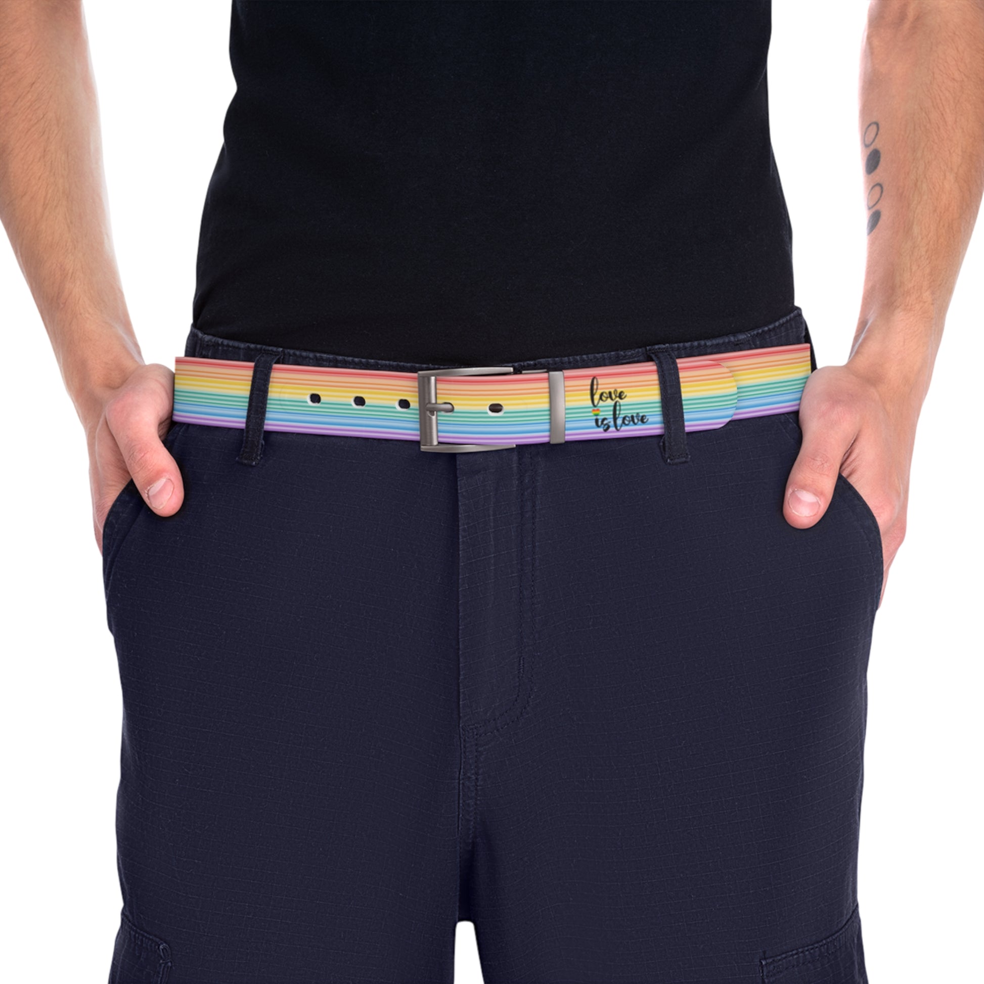 A person wearing a black shirt and black slacks with the Worldwide-PRIDE rainbow-striped Love is Love belt with gun metal buckle, showing support for the LGBTQ+ community, with one hand in their pocket.