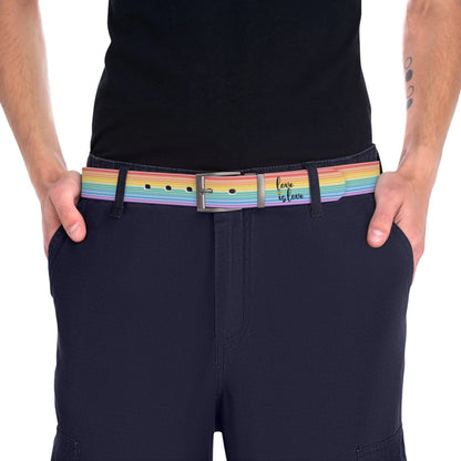 A person wearing a black shirt and black slacks with the Worldwide-PRIDE rainbow-striped Love is Love belt with gun metal buckle, showing support for the LGBTQ+ community, with one hand in their pocket.