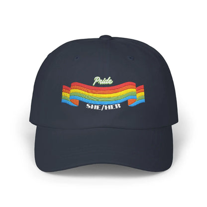 A navy blue cap from the Worldwide PRIDE store, featuring a rainbow design and the embroidered pronouns she/her.