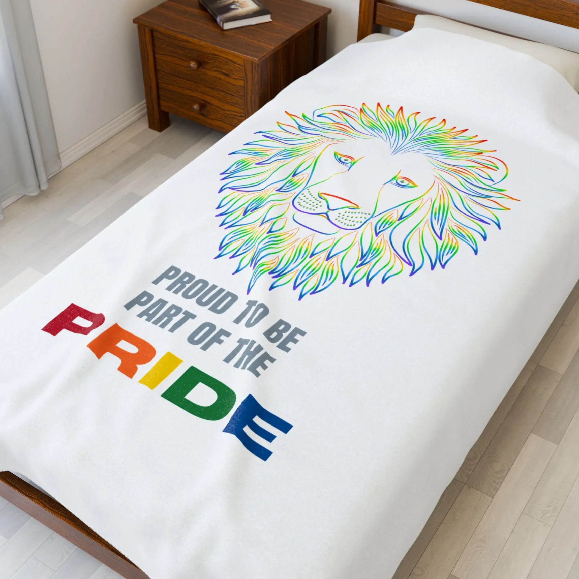 White blanket with rainbow lion design and 'Proud to be part of the Pride' text on a bed.