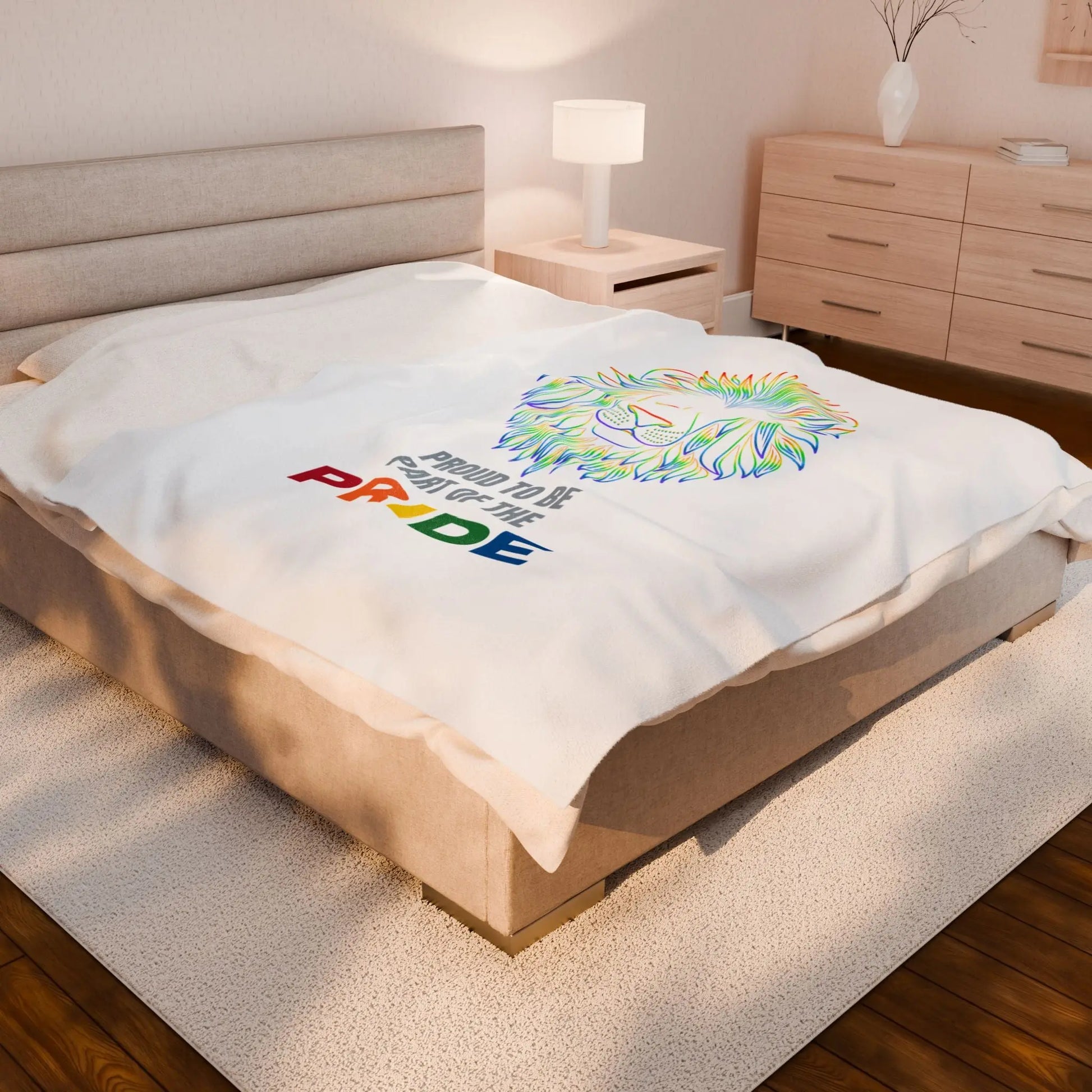 White throw blanket with rainbow lion design and 'Proud to be part of the Pride' text on a bed.