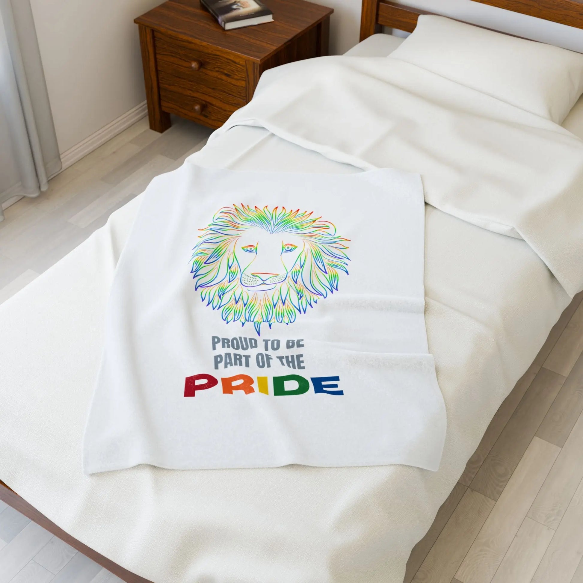 White throw blanket with rainbow lion design and 'Proud to be part of the Pride' text on a bed.