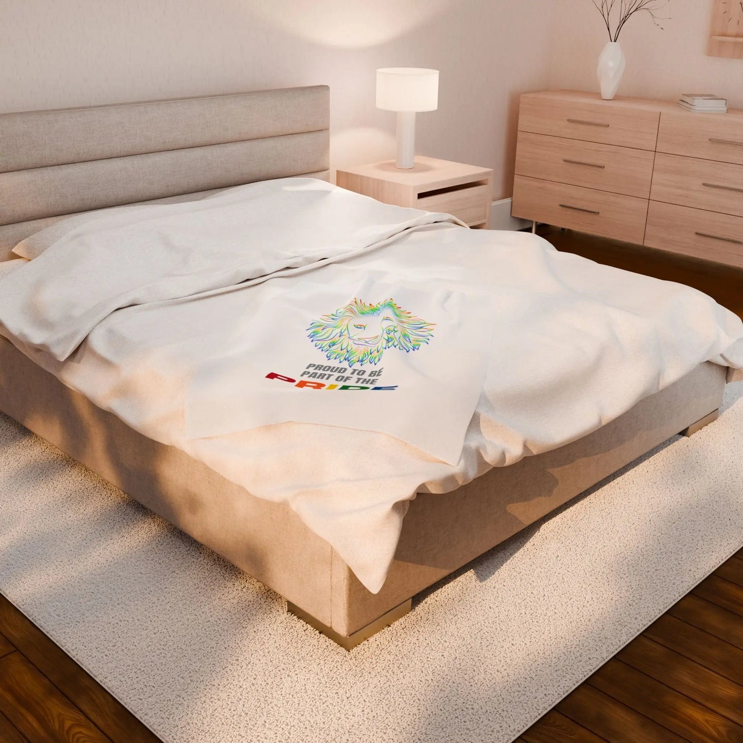 White throw blanket with rainbow lion design and 'Proud to be part of the Pride' text on a bed.