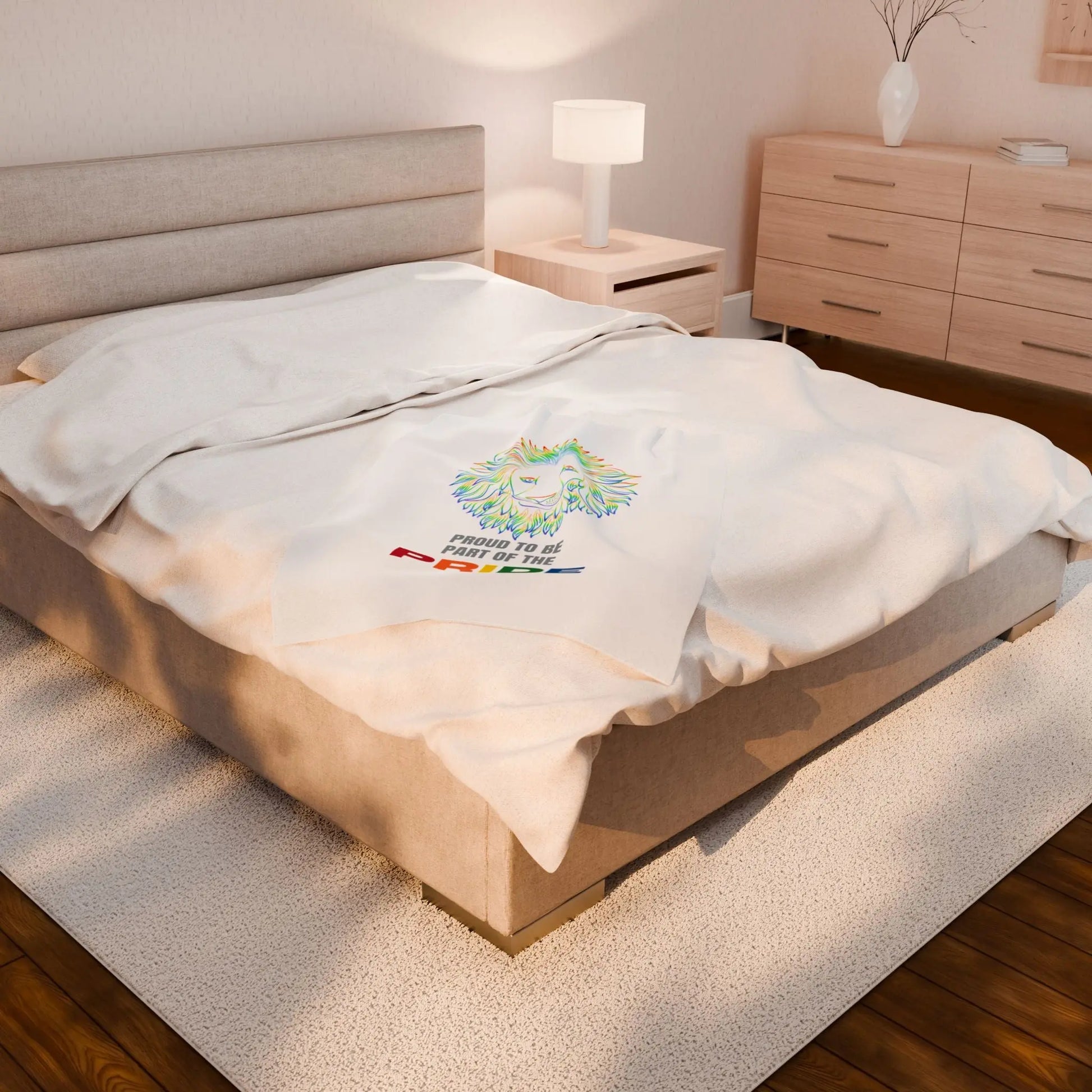 White throw blanket with rainbow lion design and 'Proud to be part of the Pride' text on a bed.