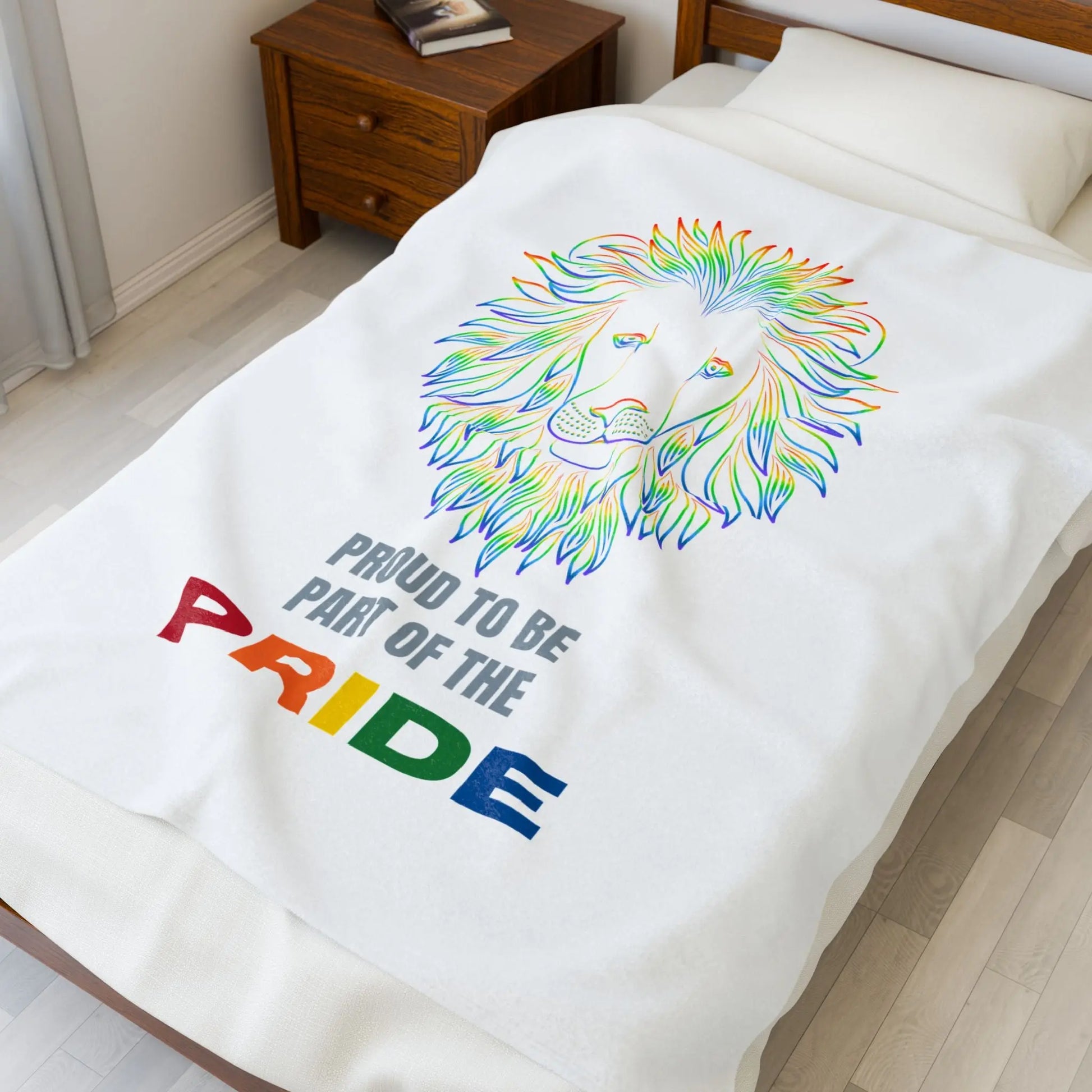 White throw blanket with rainbow lion design and 'Proud to be part of the Pride' text on a bed.