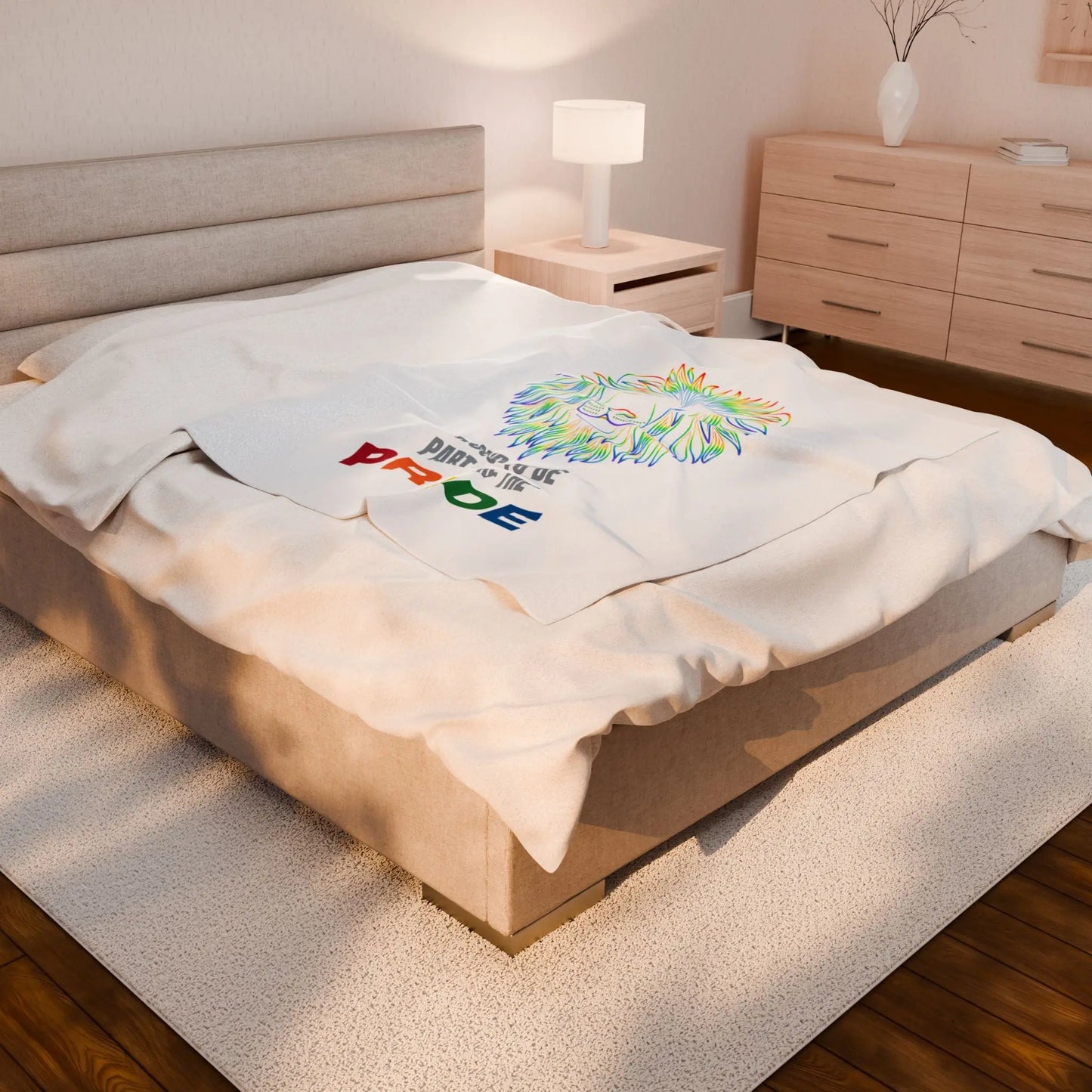White throw blanket with rainbow lion design and 'Proud to be part of the Pride' text on a bed.