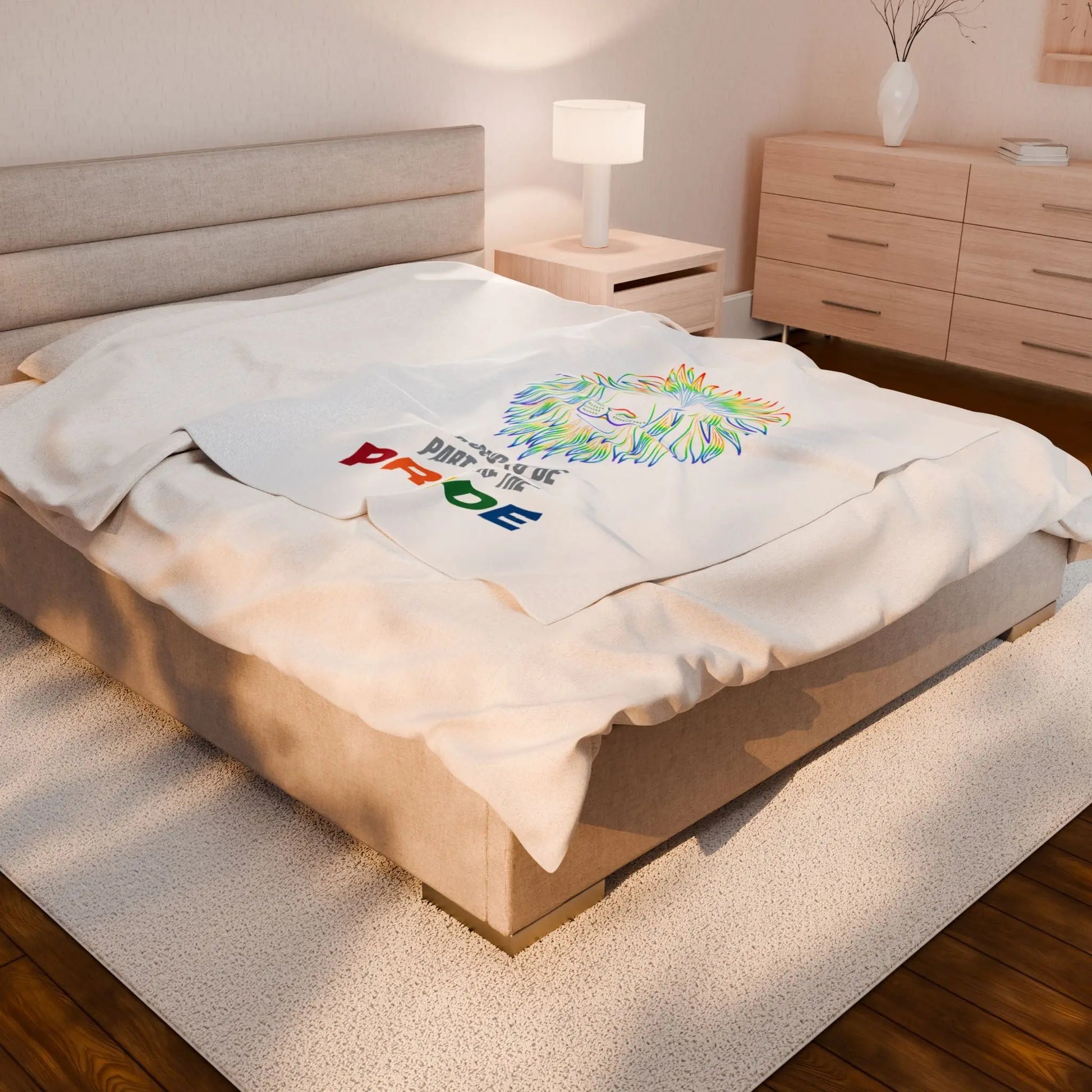 White throw blanket with rainbow lion design and 'Proud to be part of the Pride' text on a bed.