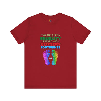 A red unisex short-sleeve t-shirt with a graphic of multicolored glitter footprints and the text 'THE ROAD TO EQUALITY IS LITTERED WITH GLITTERY FOOTPRINTS'.