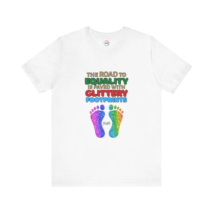 A white unisex short-sleeve t-shirt with a graphic of multicolored glitter footprints and the text 'THE ROAD TO EQUALITY IS LITTERED WITH GLITTERY FOOTPRINTS'.