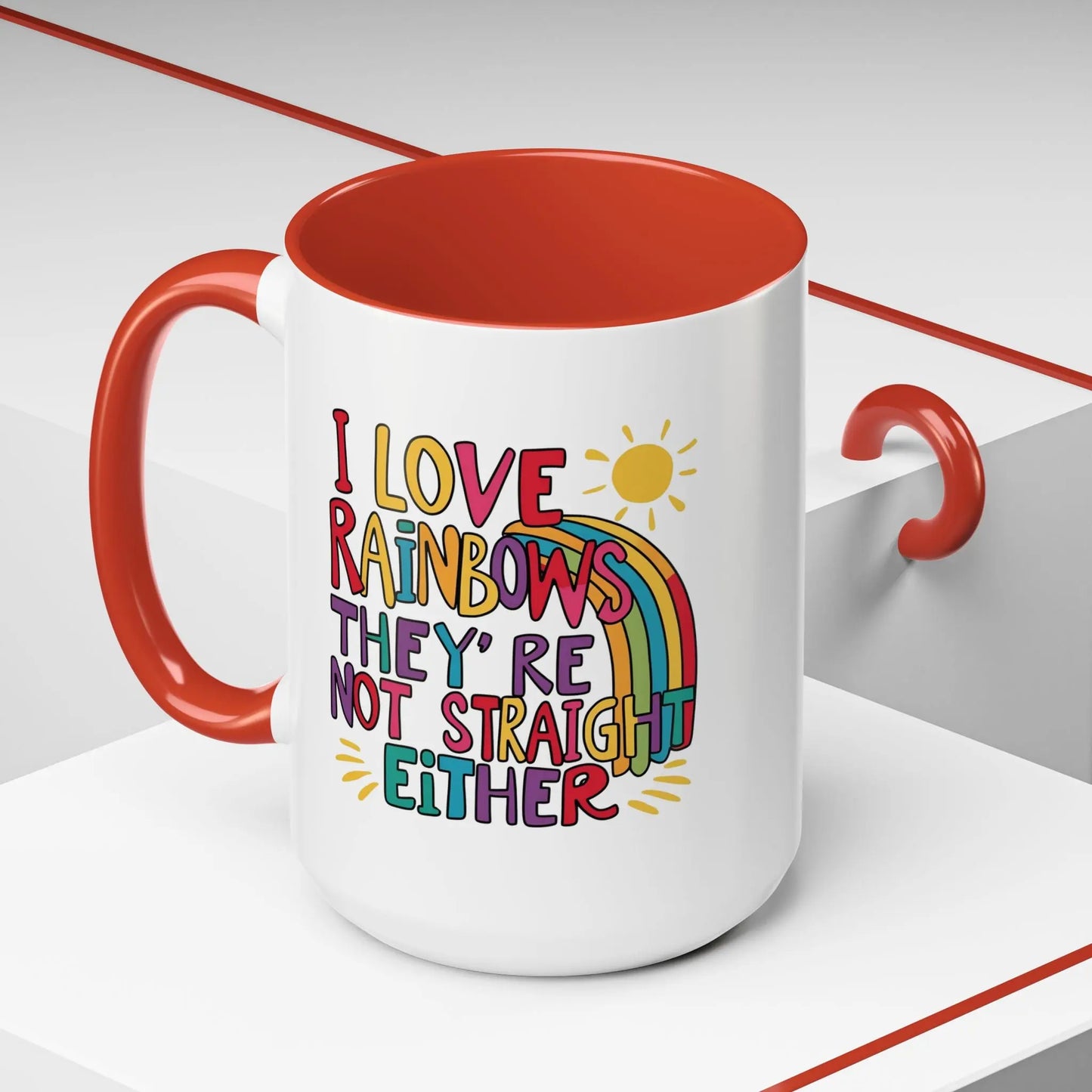 A white ceramic coffee mug with a red handle and interior, featuring the colorful text 'I LOVE RAINBOWS THEY'RE NOT STRAIGHT EITHER' along with a graphic of a rainbow and a sun.